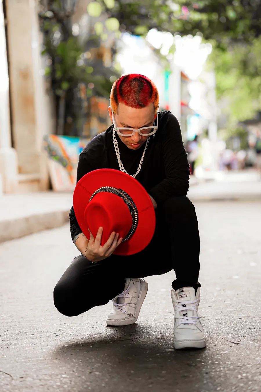 El Rocha agachado con sombrero rojo en la calle