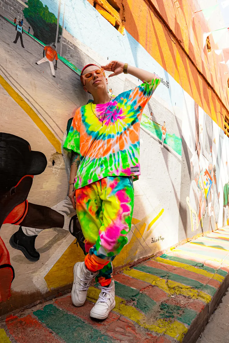 El Rocha con ropa tie-dye frente a un mural